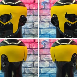 K&ouml;nnte beinhalten: Eine leuchtend gelbe Superheldenmaske mit glatter, einfarbiger Oberfl&auml;che und Aussparungen f&uuml;r die Augen. Die Maske umschlie&szlig;t den Kopf, bedeckt Stirn und Schl&auml;fen und wird auf einem schwarzen Schaufensterpuppenkopf aus verschiedenen Winkeln gezeigt.