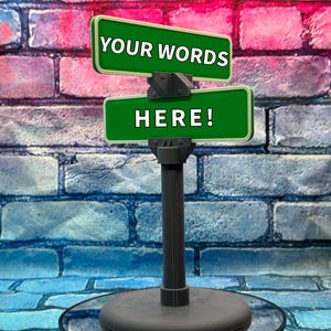 May include: A dark gray sign post with two green signs that read "YOUR WORDS" and "HERE!" in white text. The background is a brick wall with red, pink, and blue bricks.