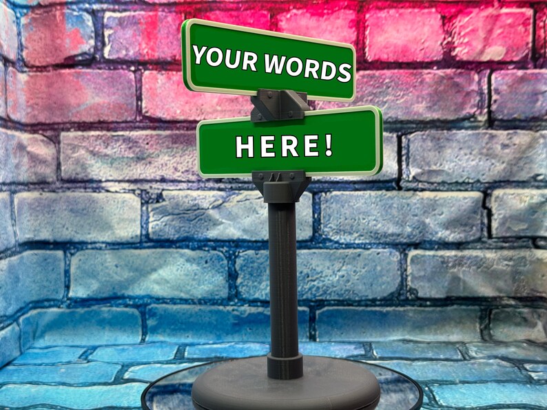 May include: A dark gray sign post with two green signs that read "YOUR WORDS" and "HERE!" in white text. The background is a brick wall with red, pink, and blue bricks.