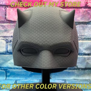Puede incluir: Una m&aacute;scara de superh&eacute;roe gris con dos cuernos puntiagudos, cubiertas de malla para los ojos y una superficie texturizada. El texto "CHECK OUT MY STORE" y "FOR OTHER COLOR VERSIONS!" se muestran en amarillo.