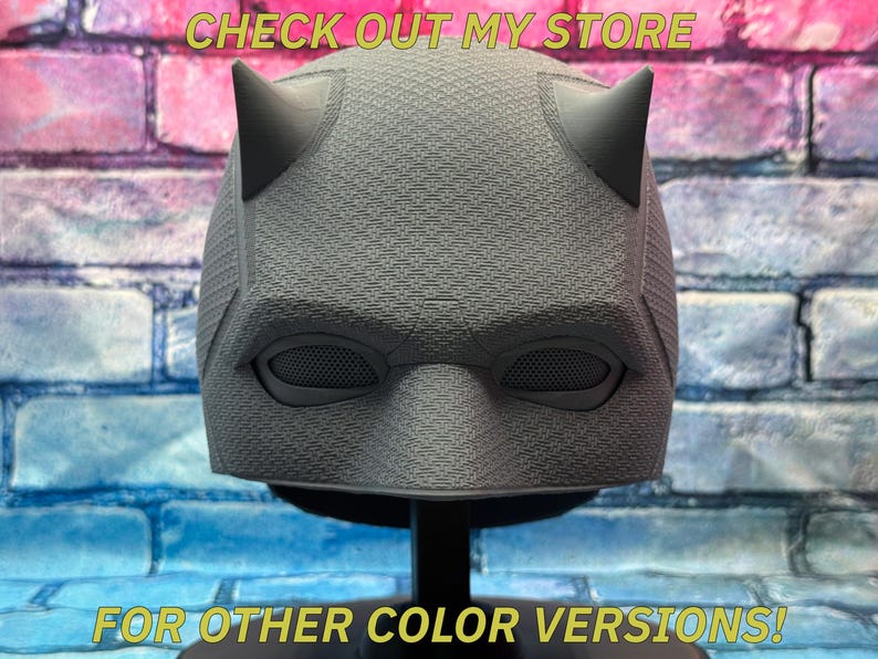 Puede incluir: Una m&aacute;scara de superh&eacute;roe gris con dos cuernos puntiagudos, cubiertas de malla para los ojos y una superficie texturizada. El texto "CHECK OUT MY STORE" y "FOR OTHER COLOR VERSIONS!" se muestran en amarillo.