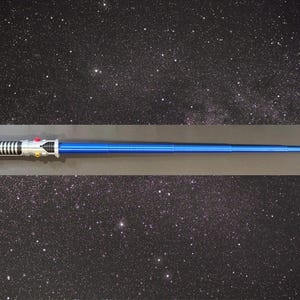 May include: A blue lightsaber prop with a silver and black handle. The prop is displayed against a starry background. The lightsaber has a long, cylindrical blue blade and detailed handle.