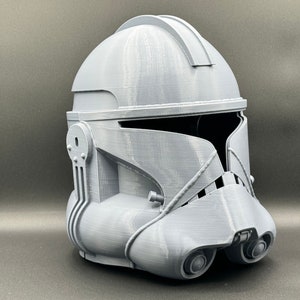 Puede incluir: Un casco gris de pl&aacute;stico impreso en 3D con una visera y una superficie texturizada. El casco est&aacute; dise&ntilde;ado para parecerse a un casco de soldado clon de Star Wars.