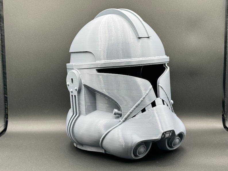Puede incluir: Un casco gris de pl&aacute;stico impreso en 3D con una visera y una superficie texturizada. El casco est&aacute; dise&ntilde;ado para parecerse a un casco de soldado clon de Star Wars.