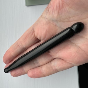 May include: A black, smooth, rounded, and slightly tapered Gua Sha tool made of jade or obsidian.