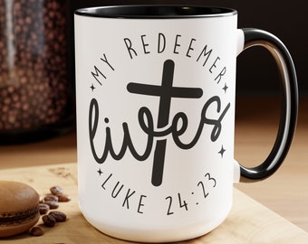 Peut inclure: Une tasse en céramique blanche avec un bord et une poignée noirs. La tasse présente un motif noir et blanc avec une croix et le texte "My Redeemer Lives Luke 24:23".