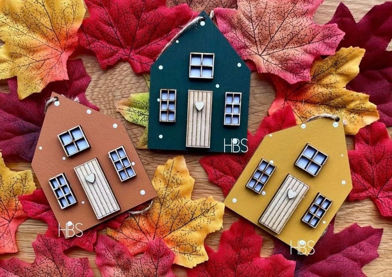 Pu&ograve; includere: Tre ornamenti a forma di casa in verde scuro, marrone e giallo senape. Ognuno presenta una porta chiara con un piccolo cuore, tre finestre con vetri bianchi e puntini bianchi. Ogni ornamento &egrave; contrassegnato con le lettere HBS.