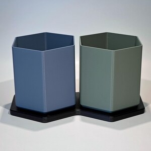 Puede incluir: Dos macetas hexagonales, una azul y otra verde, con una base hexagonal negra.