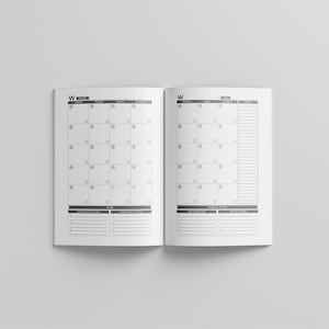 May include: Open planner with a monthly calendar layout. The pages are white with a gray grid for the calendar and space for notes. The planner is open to a month view with the days of the week across the top.