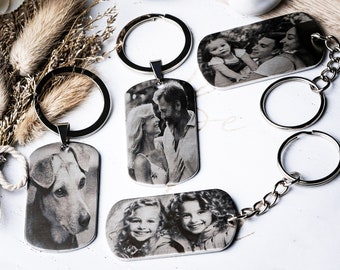 May include: Four rectangular metal keychains featuring black and white laser-engraved photographs. Three keychains have circular split rings, and one features a chain link attachment. The images depict a dog, a couple, and two children.