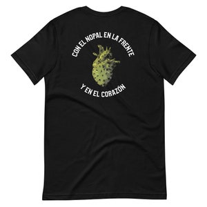 Może przedstawiać: Czarny T-shirt z białym nadrukiem w kształcie serca kaktusa z tekstem "Con el nopal en la frente y en el corazón" wokół niego.