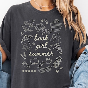 May include: A dark gray t-shirt with a white graphic design of summer-themed doodles and the text "book girl summer".