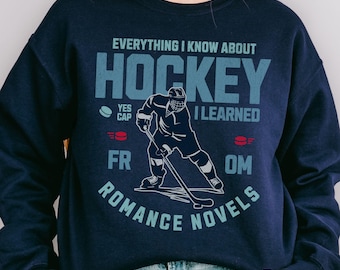 May include: Navy blue sweatshirt with the text "EVERYTHING I KNOW ABOUT HOCKEY I LEARNED FROM ROMANCE NOVELS." The design includes a hockey player graphic and the words "YES CAP" and "FR OM."