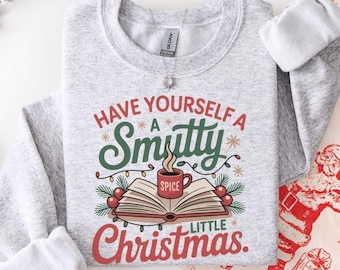 May include: A light gray sweatshirt with the text "Have Yourself A Smutty Little Christmas" in red and green. The graphic includes an open book, a mug of spice, and Christmas lights. A festive holiday sweater.