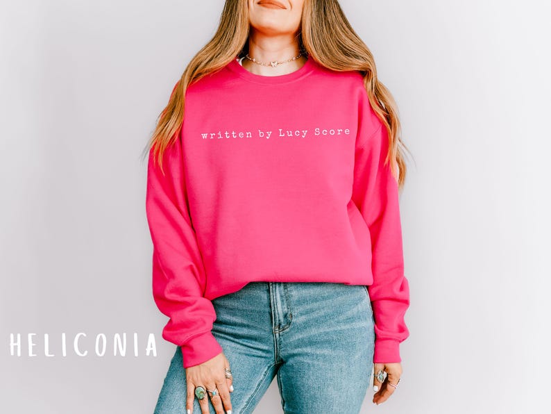 May include: A bright pink sweatshirt with the text "written by Lucy Score" in white.