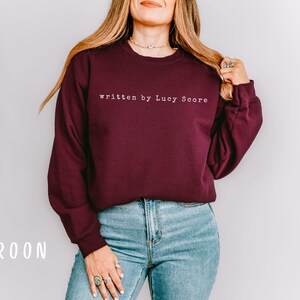 May include: A maroon sweatshirt with the text "written by Lucy Score" in white.