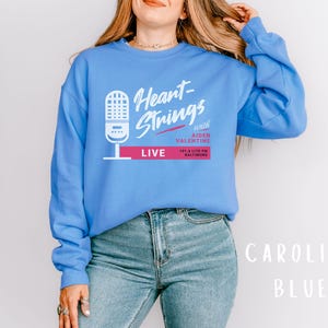 Puede incluir: Una sudadera azul con el texto "Heart-Strings with Aiden Valentine LIVE 101.5 Lite FM Baltimore" impreso en la parte delantera.