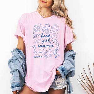 May include: A pink t-shirt with a blue graphic design of summer-themed doodles and the text "book girl summer".