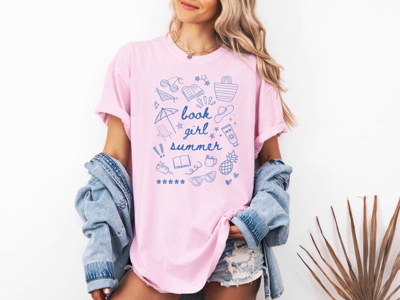 May include: A pink t-shirt with a blue graphic design of summer-themed doodles and the text "book girl summer".