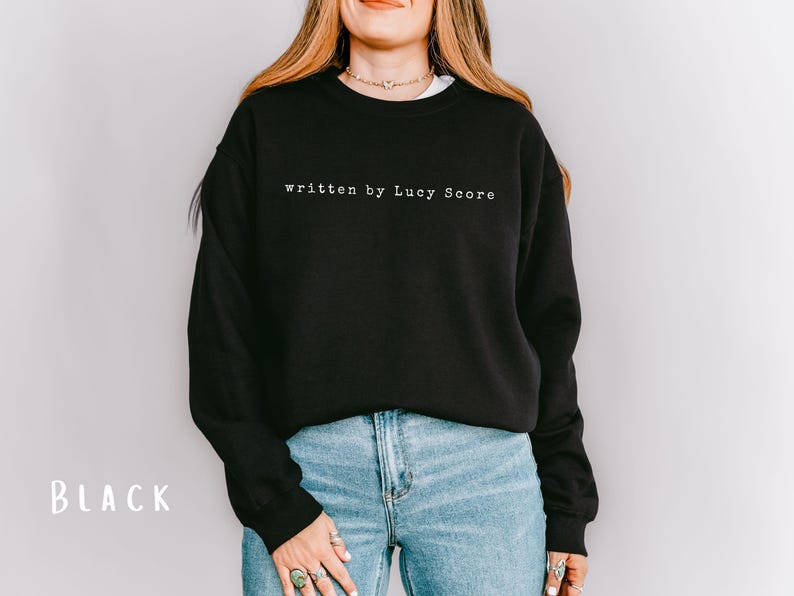 May include: Black sweatshirt with the text "written by Lucy Score" in white.