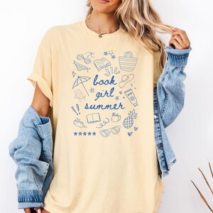 May include: A yellow t-shirt with a blue graphic design of summer-themed doodles and the text "book girl summer".