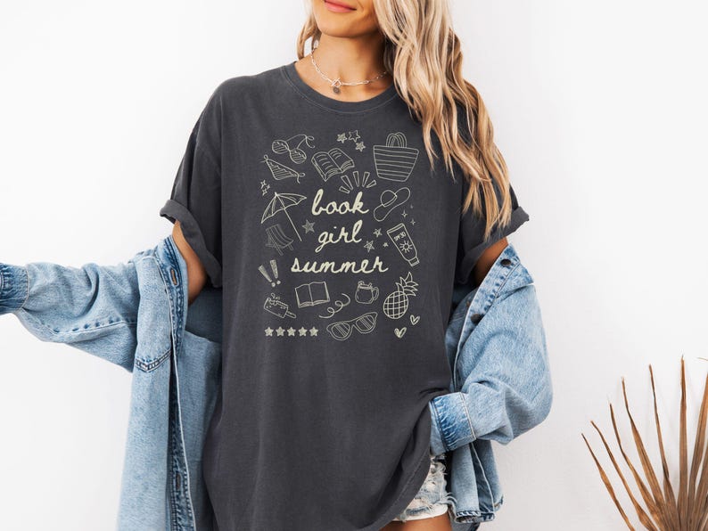 May include: A dark gray t-shirt with a white graphic design of summer-themed doodles and the text "book girl summer".