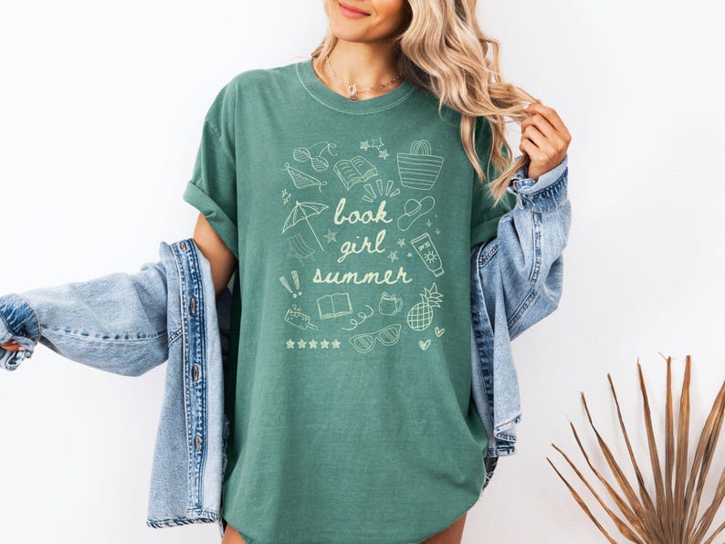 May include: A green t-shirt with a white graphic design of summer-themed doodles and the text "book girl summer".