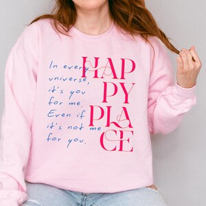 Może przedstawiać: R&oacute;żowa bluza z napisem "In every universe, it's you for me. Even if it's not me for you. Happy Place" w r&oacute;żowych i niebieskich literach.