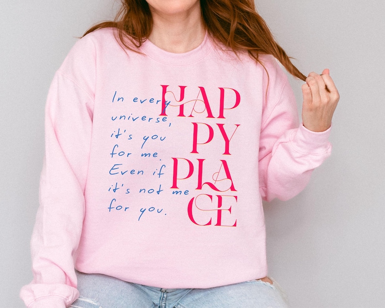 Może przedstawiać: R&oacute;żowa bluza z napisem "In every universe, it's you for me. Even if it's not me for you. Happy Place" w r&oacute;żowych i niebieskich literach.