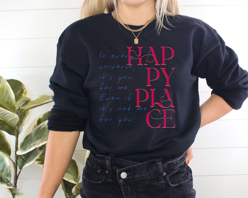 Może przedstawiać: Czarna bluza z nadrukiem "In every universe, it's you for me. Even if it's not me for you. Happy Place" w czerwonym i niebieskim kolorze.