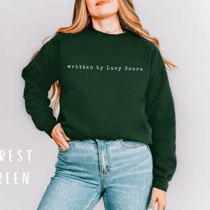 May include: A forest green sweatshirt with the text "written by Lucy Score" in white.