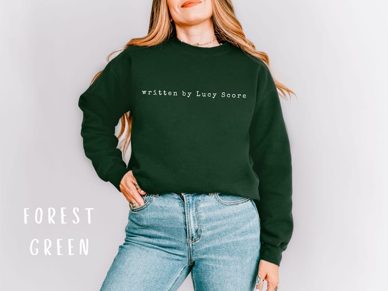 May include: A forest green sweatshirt with the text "written by Lucy Score" in white.