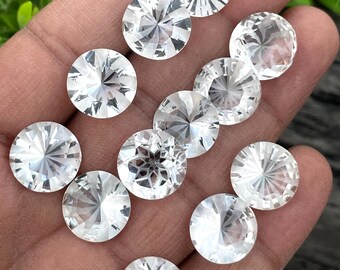Puede incluir: Una colección de gemas redondas, facetadas y transparentes. Las gemas se sostienen en una mano, mostrando su corte brillante y superficies reflectantes. Las gemas están dispuestas en un patrón disperso, con tamaños y ángulos variables, creando una exhibición brillante.