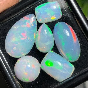 May include: Six iridescent opal gemstones in various shapes and sizes, including teardrop, oval, and rectangular, with a rainbow of colors, including green, blue, pink, and orange.