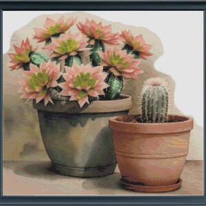 May include: A framed artwork featuring two potted cacti. The larger pot, painted in a muted green, holds a cactus with multiple pink and green blooms. A smaller terracotta pot contains a single, spiky cactus.