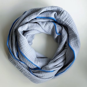 Könnte beinhalten: Ein grauer Loop-Schal mit blauen Nähten an den Kanten. Der Schal besteht aus einem weichen, strukturierten Stoff und ist in einer kreisförmigen Form geschlungen. Die blauen Nähte bilden einen Kontrast zum grauen Stoff.