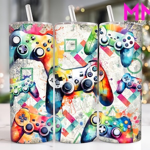 May include: Three colourful stainless steel tumblers with a design of video game controllers on a white background with colourful paint splatters. The tumblers are 20 ounces each.
