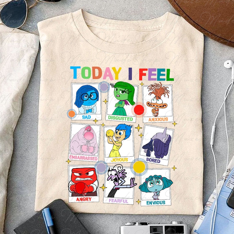 May include: A beige t-shirt with the words 'TODAY I FEEL' printed on the front. Below the words are nine squares with different characters from the movie Inside Out. Each square has a different emotion written below the character. The emotions are: Sad, Disgusted, Anxious, Embarrassed, Joyous, Bored, Angry, Fearful, and Envious.
