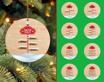 May include: A round Christmas ornament with a wood grain background. The ornament features a red signpost with the text "SMITH FAMILY" and arrows labeled "Name". Snowflakes and a snow base complete the design. Additional ornaments are shown.