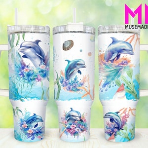 May include: White insulated tumbler featuring a watercolor design of a dolphin leaping through water, surrounded by blue and purple flowers and aquatic plants. The tumbler has a white handle and lid with a straw. The text "MUSEMADESHOP" is visible.