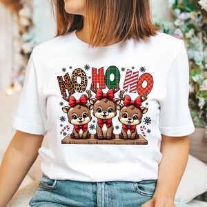 May include: White t-shirt with a Christmas design featuring three cartoon reindeer with red bows and the text "HO HO HO" in a plaid pattern.