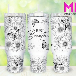 May include: White tumbler with a floral and butterfly design. The tumbler features black and white illustrations of flowers and butterflies, with the words "JUST BREATHE" in a script font. Includes a white handle and straw.