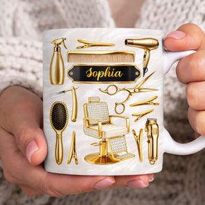 May include: A white ceramic mug with a marble pattern featuring gold-colored salon equipment illustrations including a hair dryer, scissors, comb, spray bottle, hair clips, and a barber chair. The name Sophia is printed in gold on a black plaque.