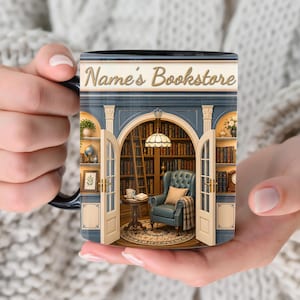 May include: A ceramic mug featuring a printed illustration of a bookstore interior with the text Name's Bookstore. The design shows a blue arched doorway, a teal armchair, a wooden side table, a lamp, and shelves filled with books.