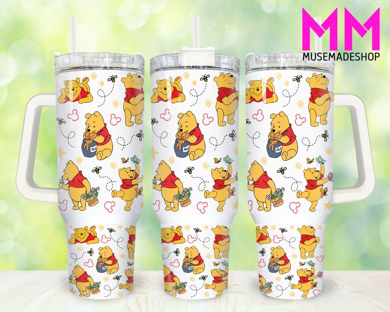 May include: Three stainless steel tumblers with a white background and a repeating pattern of Winnie the Pooh characters. The characters are yellow and red and are holding honey pots and flowers. The tumblers have a white handle and a clear lid. The text 'MM MUSEMADESHOP' is in pink letters in the top right corner of the image.