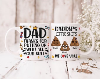 May include: Two white ceramic mugs with black text and colorful graphics. One mug says "DAD" and "THANKS FOR PUTTING UP WITH ALL OUR SHIT." The other says "DADDY'S LITTLE SHITS" with poop emojis and names.