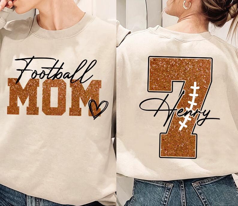 May include: Two beige sweatshirts with a football theme. One sweatshirt has the text "Football Mom" in brown glitter letters with a heart. The other sweatshirt has a brown glitter number "7" with the name "Henry" written in cursive below it.