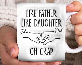 May include: White ceramic mug with black text that reads "Like father like daughter" with the names "Julia" and "Dad" written below. Two fists bump in the center of the mug with the text "Oh crap" below.