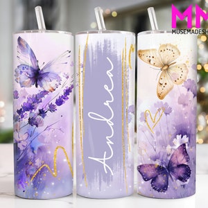 Könnte beinhalten: Drei Edelstahlbecher mit einem lila und goldenen Aquarelldesign mit Schmetterlingen und dem Namen "Andrea" auf einem der Becher.