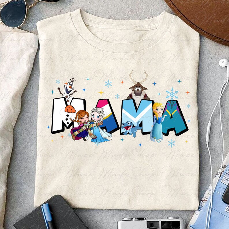 May include: A beige t-shirt with a graphic design featuring the word "MAMA" in blue, pink, and yellow letters. The letters are decorated with cartoon characters from the movie Frozen, including Olaf, Elsa, Anna, and Sven the reindeer.